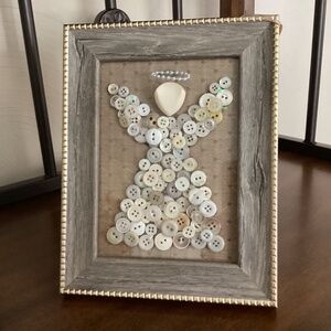 Button angel in frame. Gold fabric background. Wood like frame with gold trim.